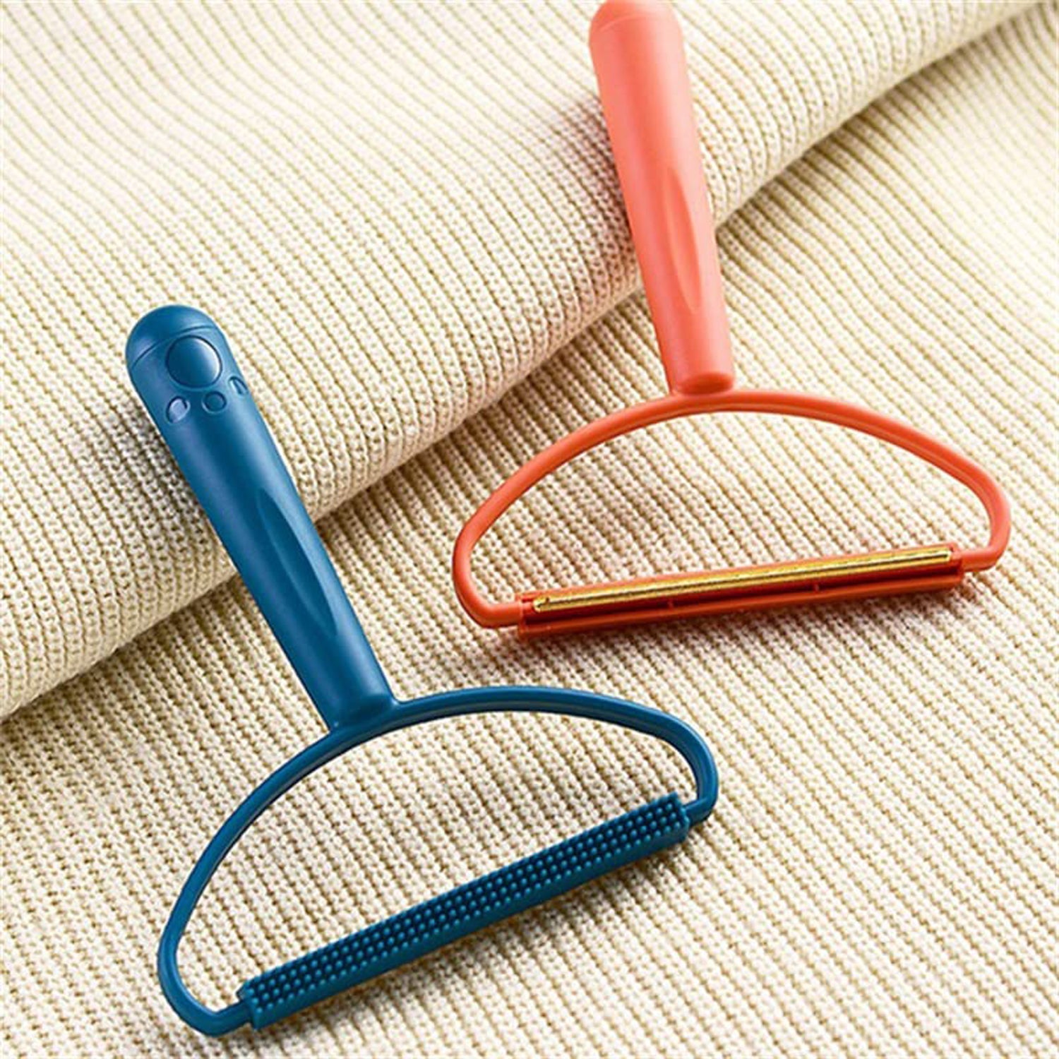 A blue fabric brush lint remover and an orange metal shaver lint remover resting on a light beige knitted fabric.