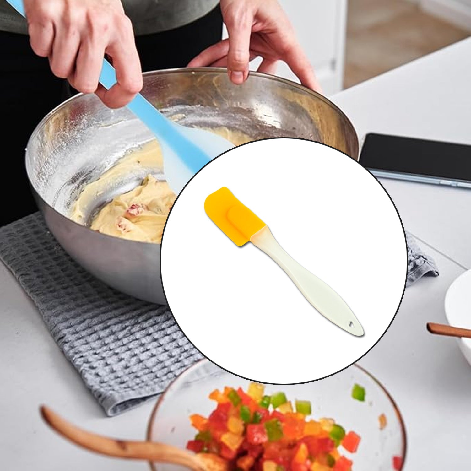 A hand uses a blue spatula to mix dough in a metal bowl, with a yellow spatula highlighted in a circular inset.