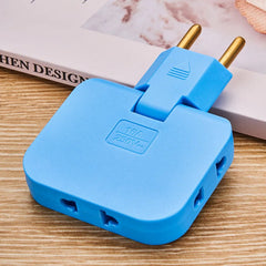 A blue 3-in-1 foldable wall plug adapter with brass pins, resting on a wooden surface next to a book.