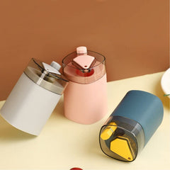 Three automatic toothpick dispensers, one grey, one pink, and one teal, are arranged on a light brown surface.