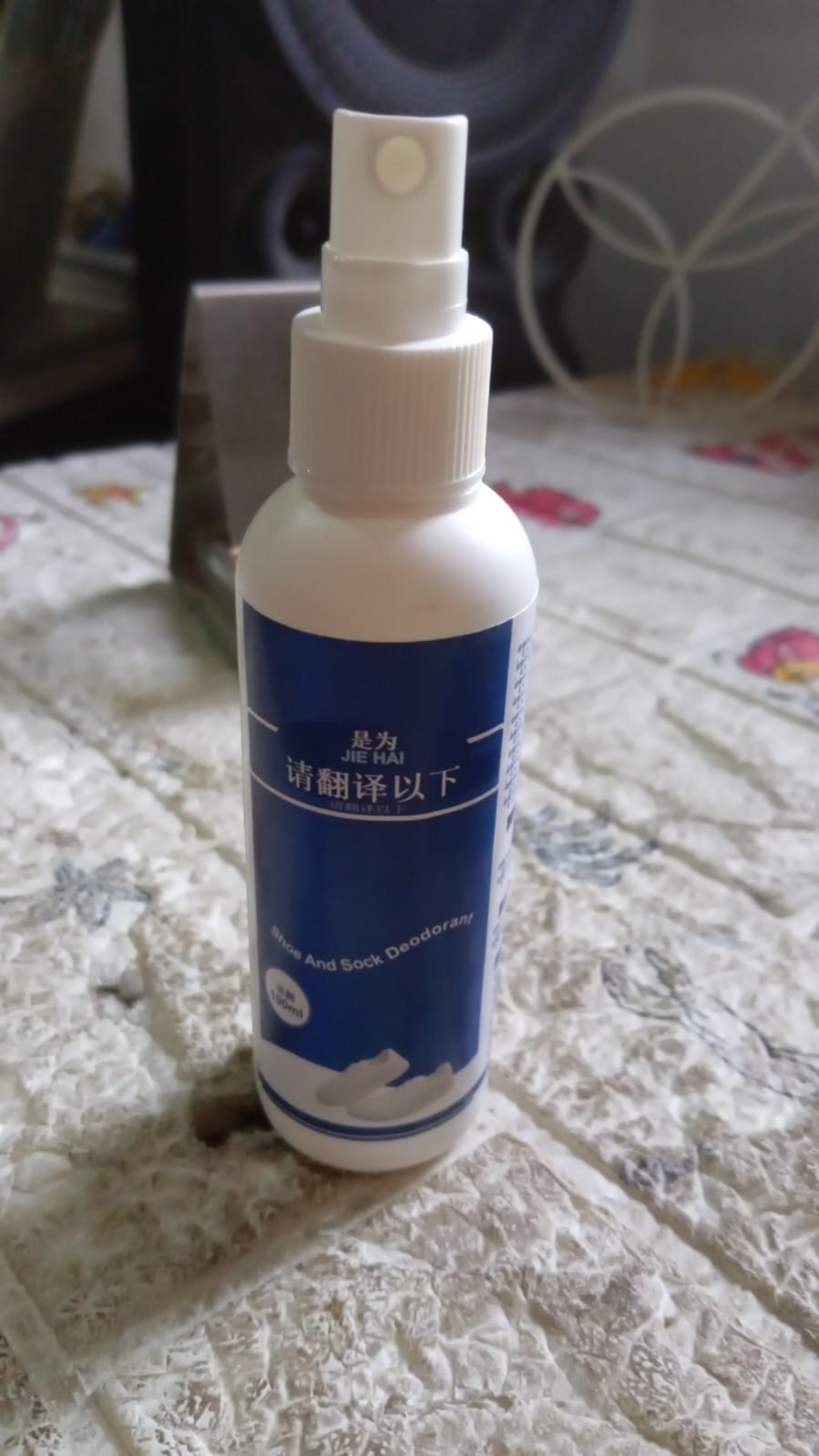 A white bottle with a blue label for shoe and sock deodorant stands on a patterned surface.