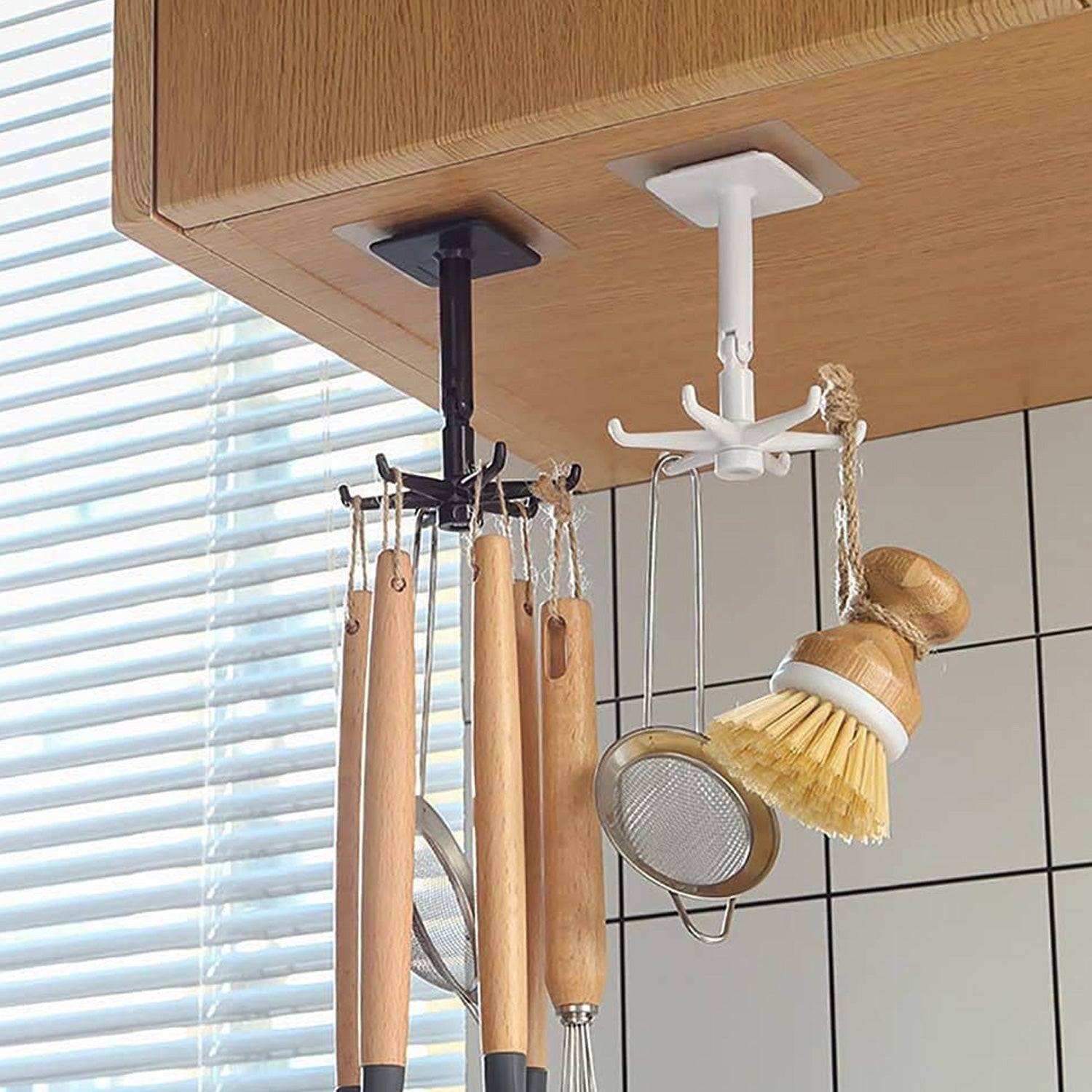Two rotating hooks, one black and one white, hang from a wooden cabinet, holding various kitchen utensils.