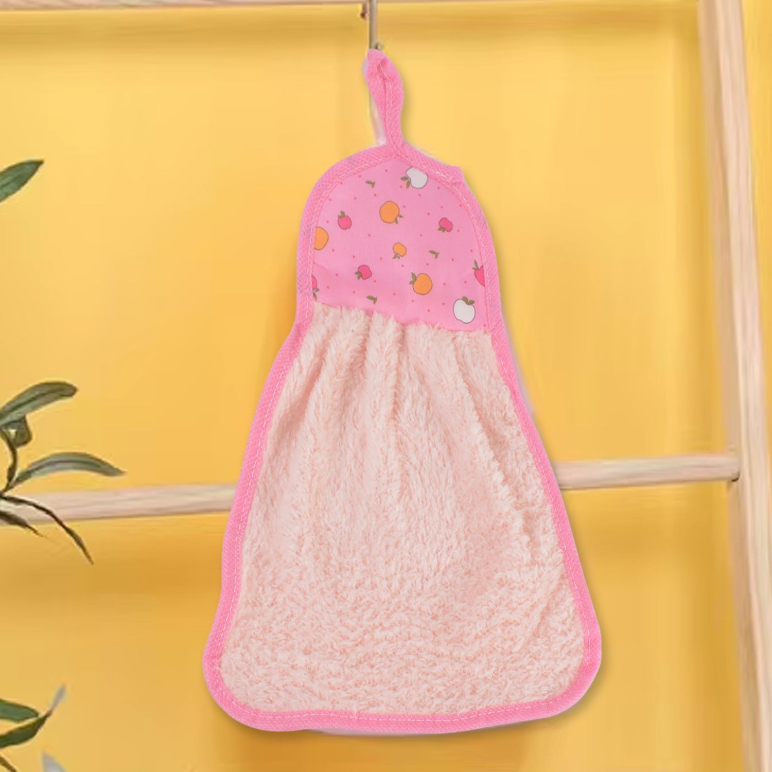 A pink microfiber hand towel with a fruit print top and hanging loop hangs from a hook against a bright yellow wall.