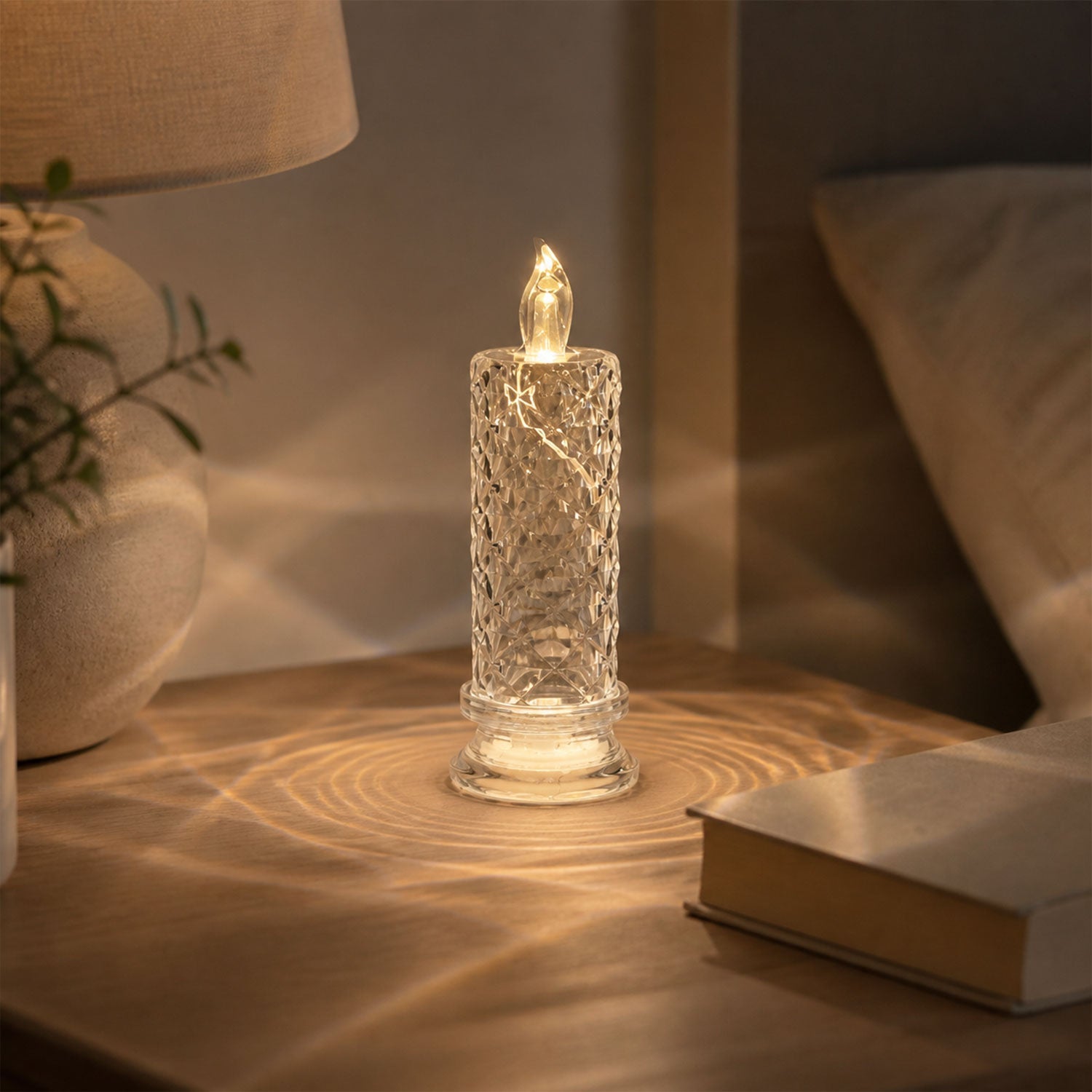 A clear faceted crystal LED candle light on a bedside table, casting warm light patterns on the surface.