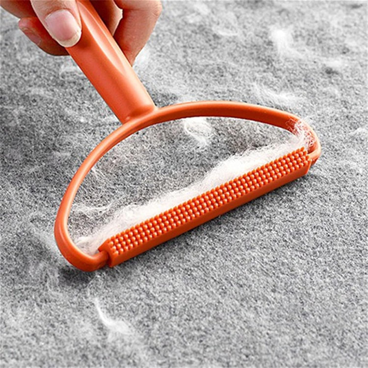 A hand holding an orange fabric brush lint remover covered in white lint on a grey textured surface.