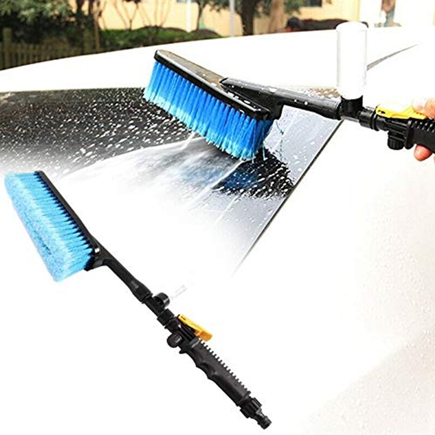 A blue car washing brush with a long handle spraying water and soap onto a white car's roof.