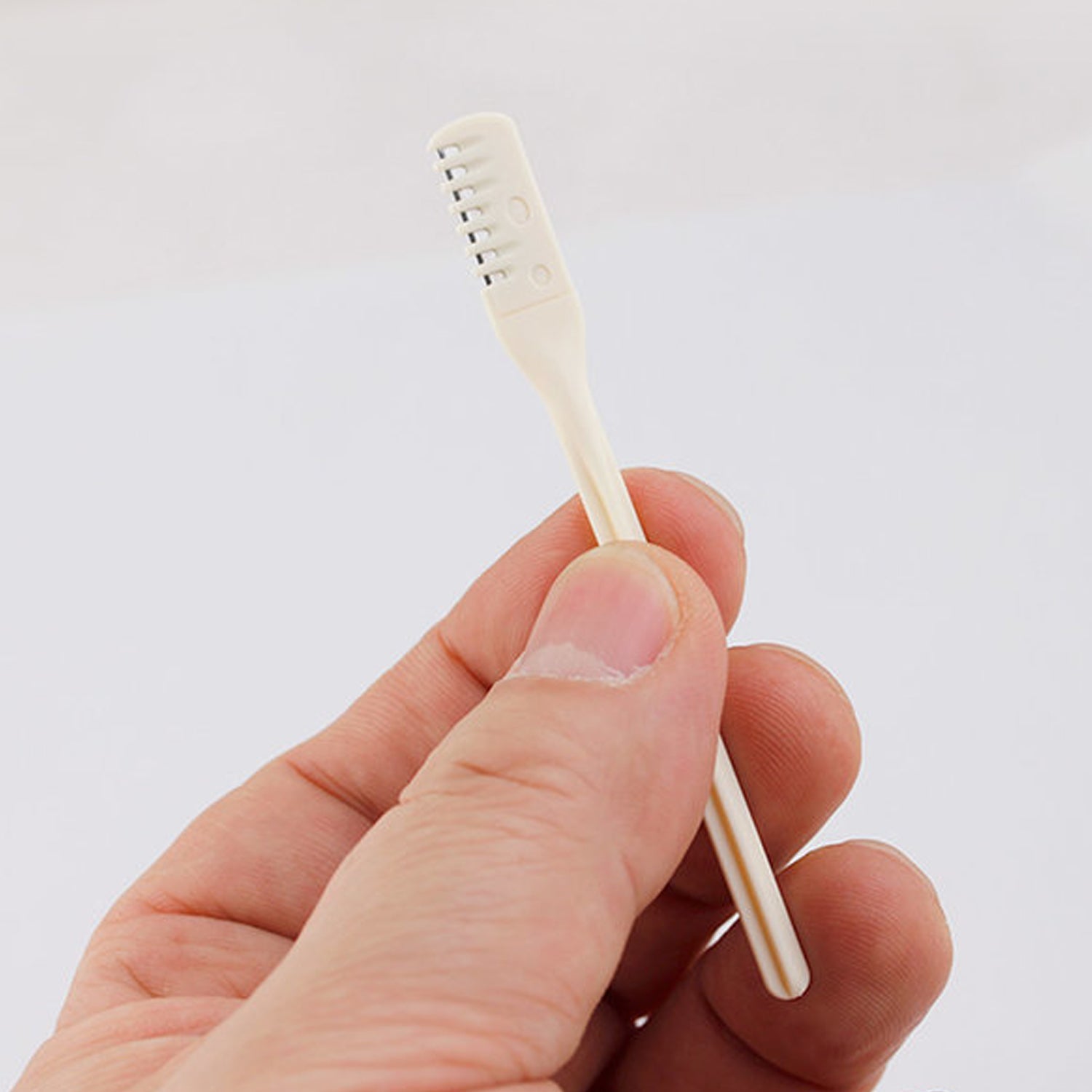 A hand holds a single beige manual nose hair trimmer with a white background.