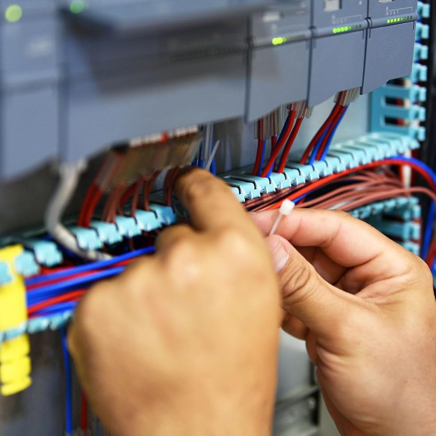 A person's hands securing a bundle of colorful wires with a white cable tie inside an electrical panel.