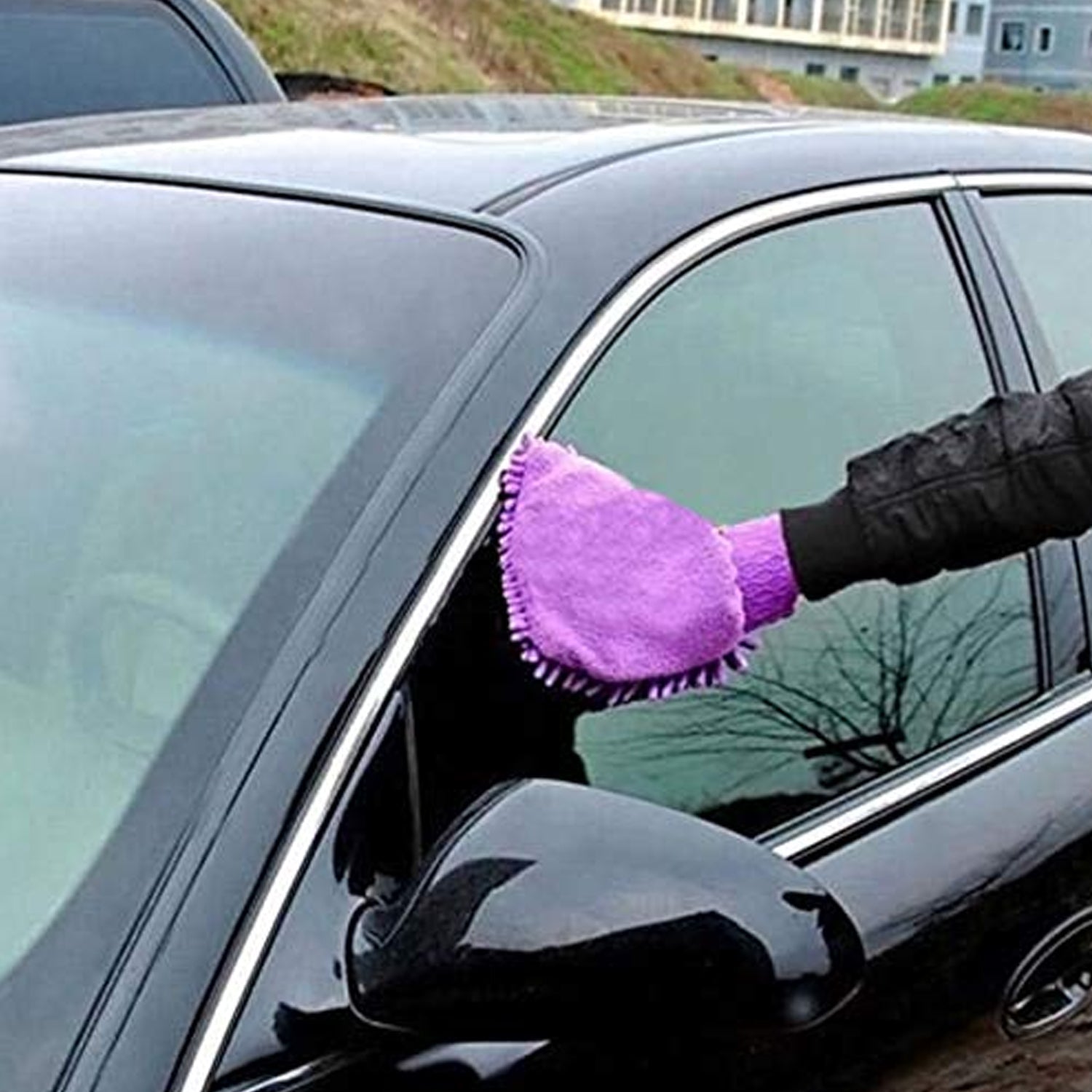 A person's hand wearing a purple chenille mitt cleaning the window frame of a black car.