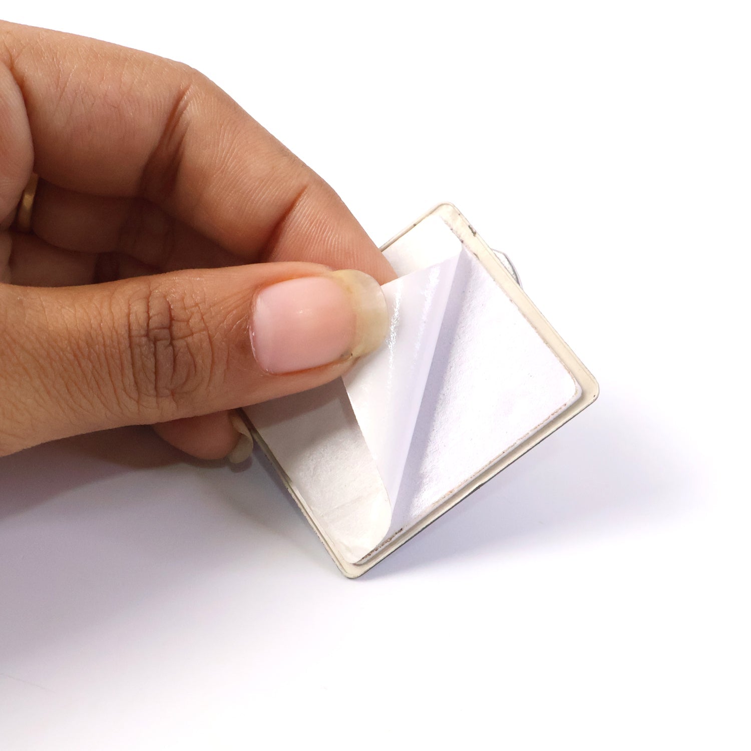 A hand peeling the protective film off the adhesive backing of a square black phone ring stand.