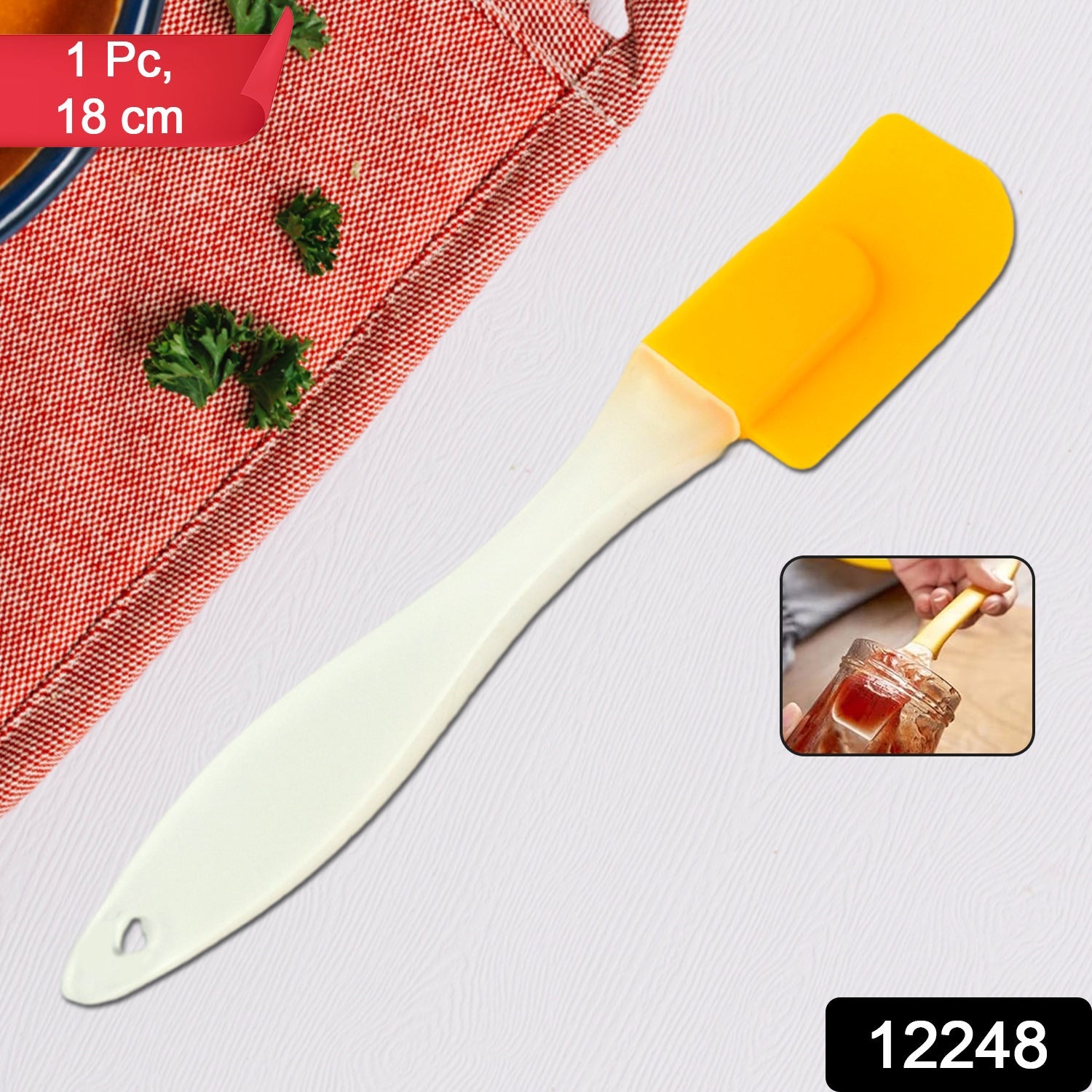 A yellow silicone spatula with a cream handle is shown on a grey background with a red patterned cloth and a small inset