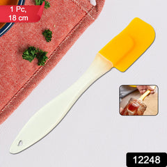 A yellow silicone spatula with a cream handle is shown on a grey background with a red patterned cloth and a small inset
