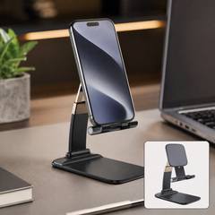 Black and gold foldable phone stand holding a smartphone on a desk next to a laptop and plant.