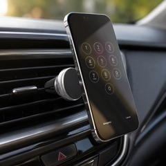 A black smartphone with a numerical keypad on its screen is held by a magnetic mount attached to a car's air vent.