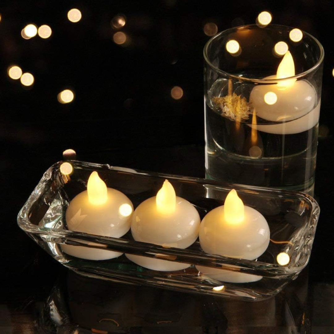 Three white LED floating candles in a clear rectangular dish and one in a tall glass, all lit.