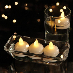 Three white LED floating candles in a clear rectangular dish and one in a tall glass, all lit.