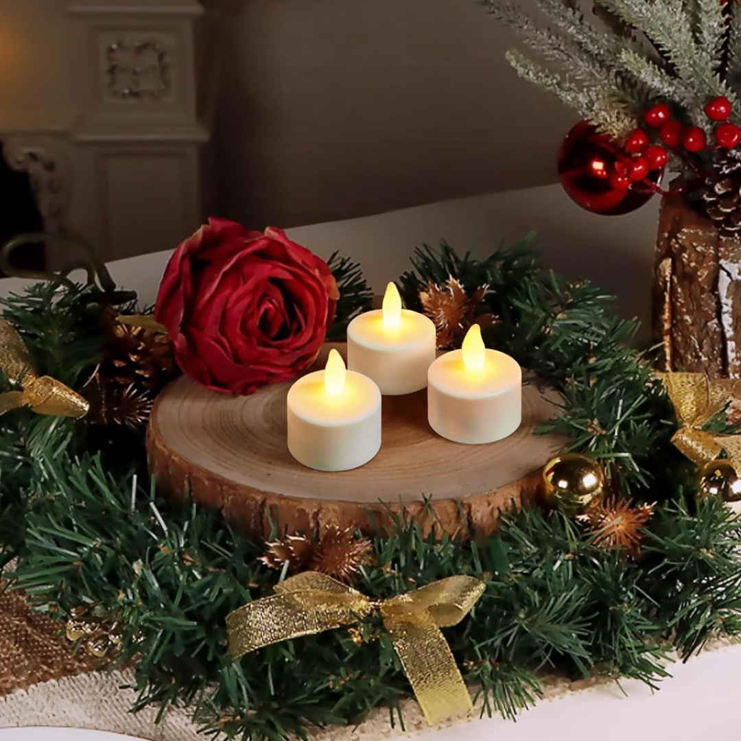 Three white LED tea lights on a wooden slice surrounded by green garland, a red rose, and gold ornaments.
