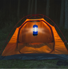 A blue lantern hangs inside an orange tent, casting a warm glow on the interior fabric and ground.
