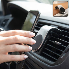A hand places a smartphone onto a silver and black magnetic car phone holder attached to an air vent.