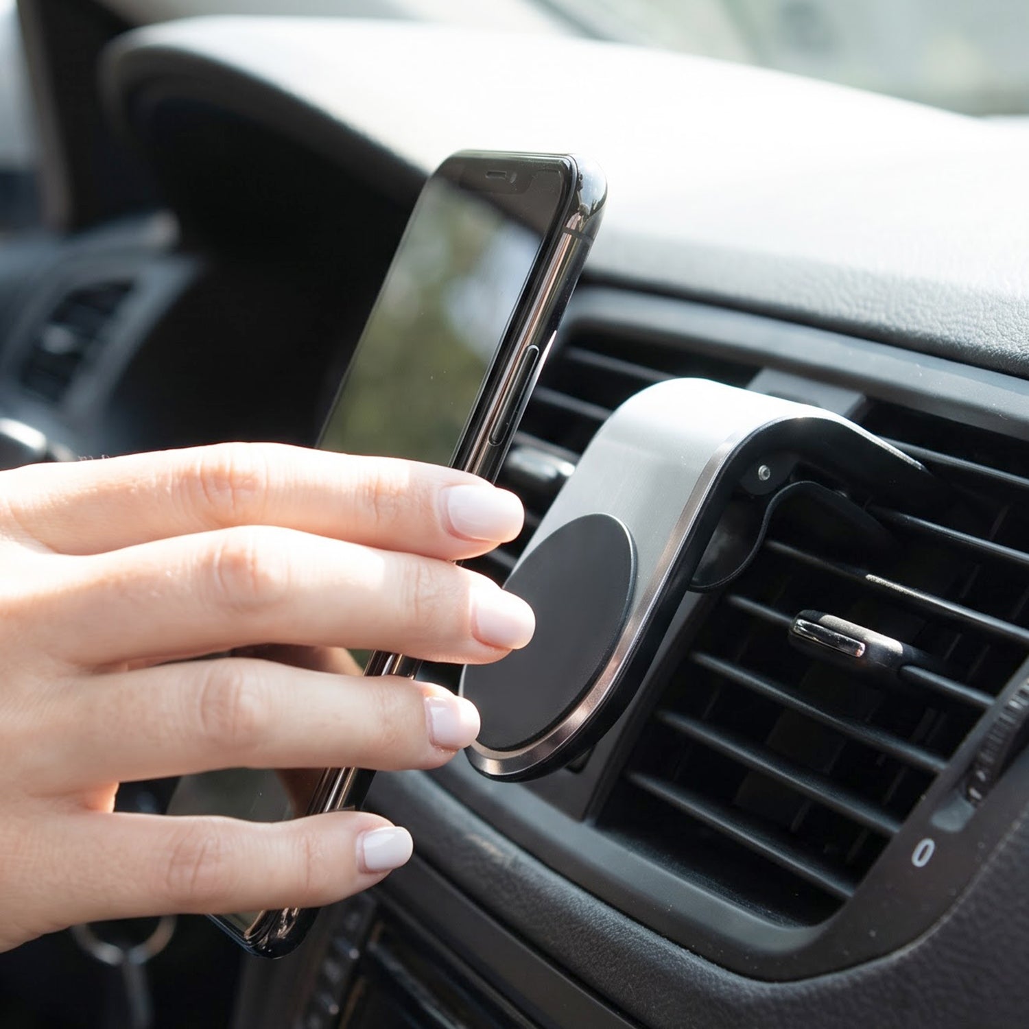 A silver and black magnetic car phone holder is shown on a light grey car interior surface.