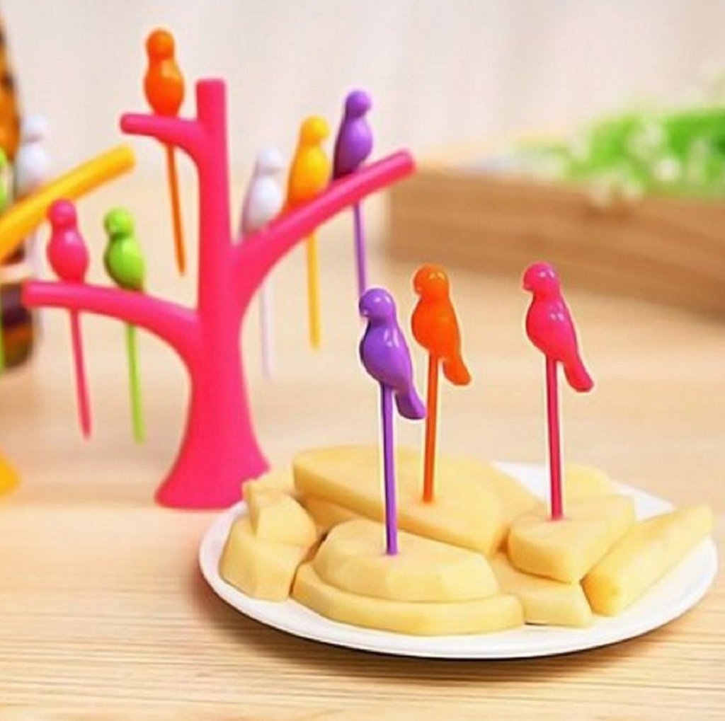 A pink tree holder with colorful bird fruit forks in cheese cubes on a white plate, with a green tree holder in the