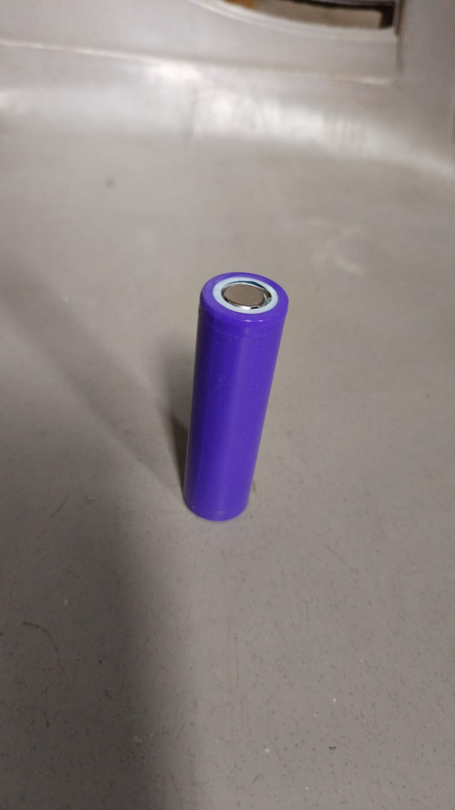A single purple battery stands upright on a textured gray surface.
