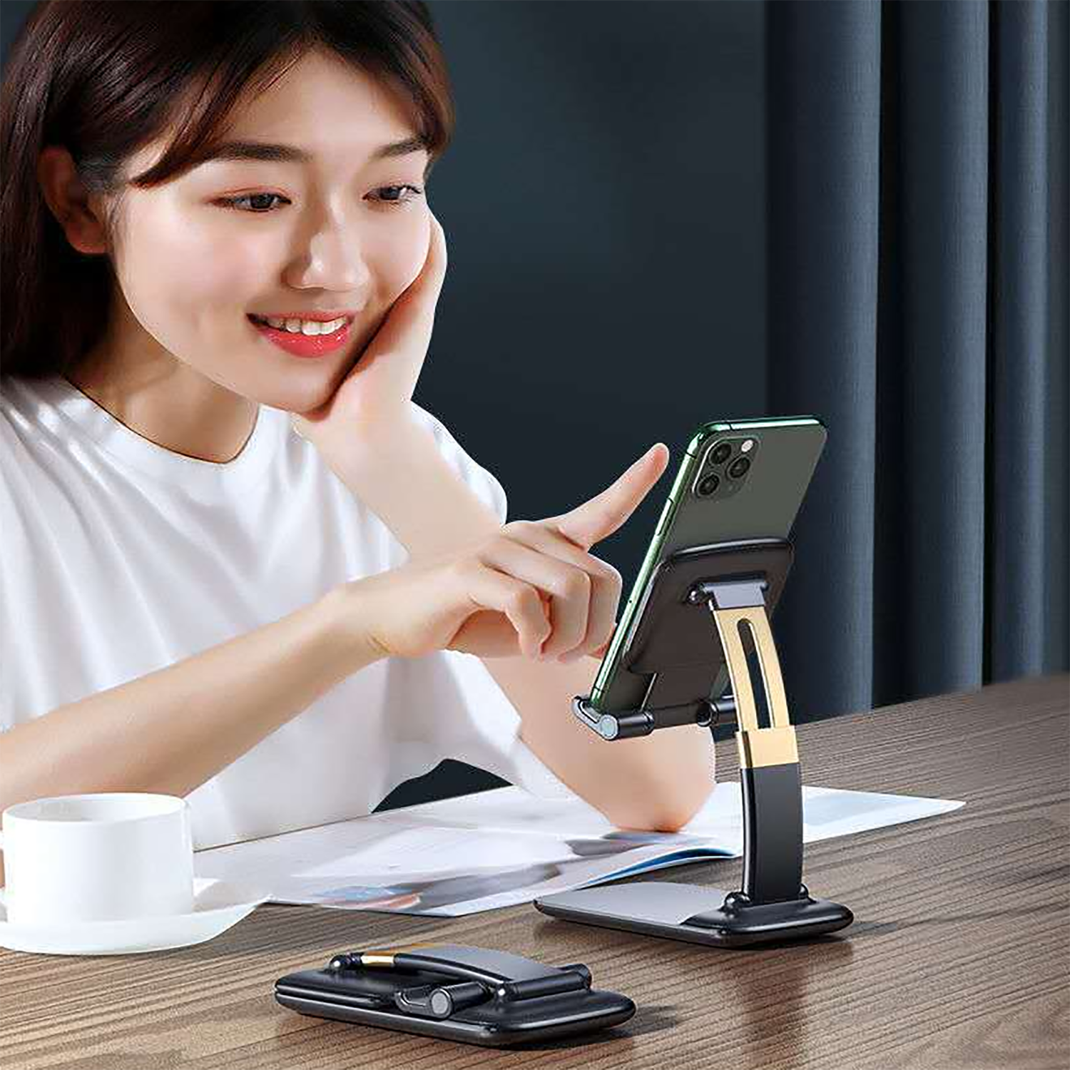 A woman smiling while interacting with a smartphone on a black and gold foldable stand, with another stand folded on the