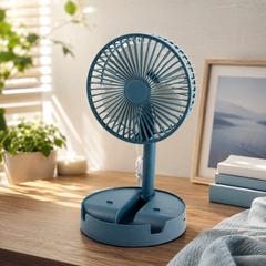 A teal portable fan with a round head and adjustable stand sits on a wooden desk next to a plant.