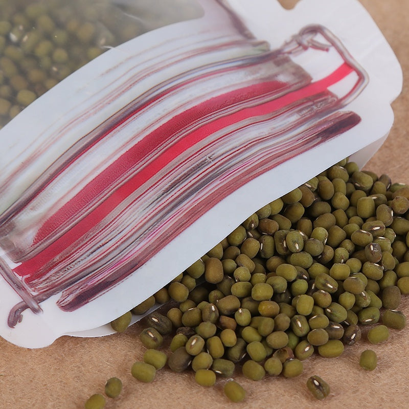 A close-up of a jar-shaped zipper pouch with green mung beans spilling out onto a brown surface.