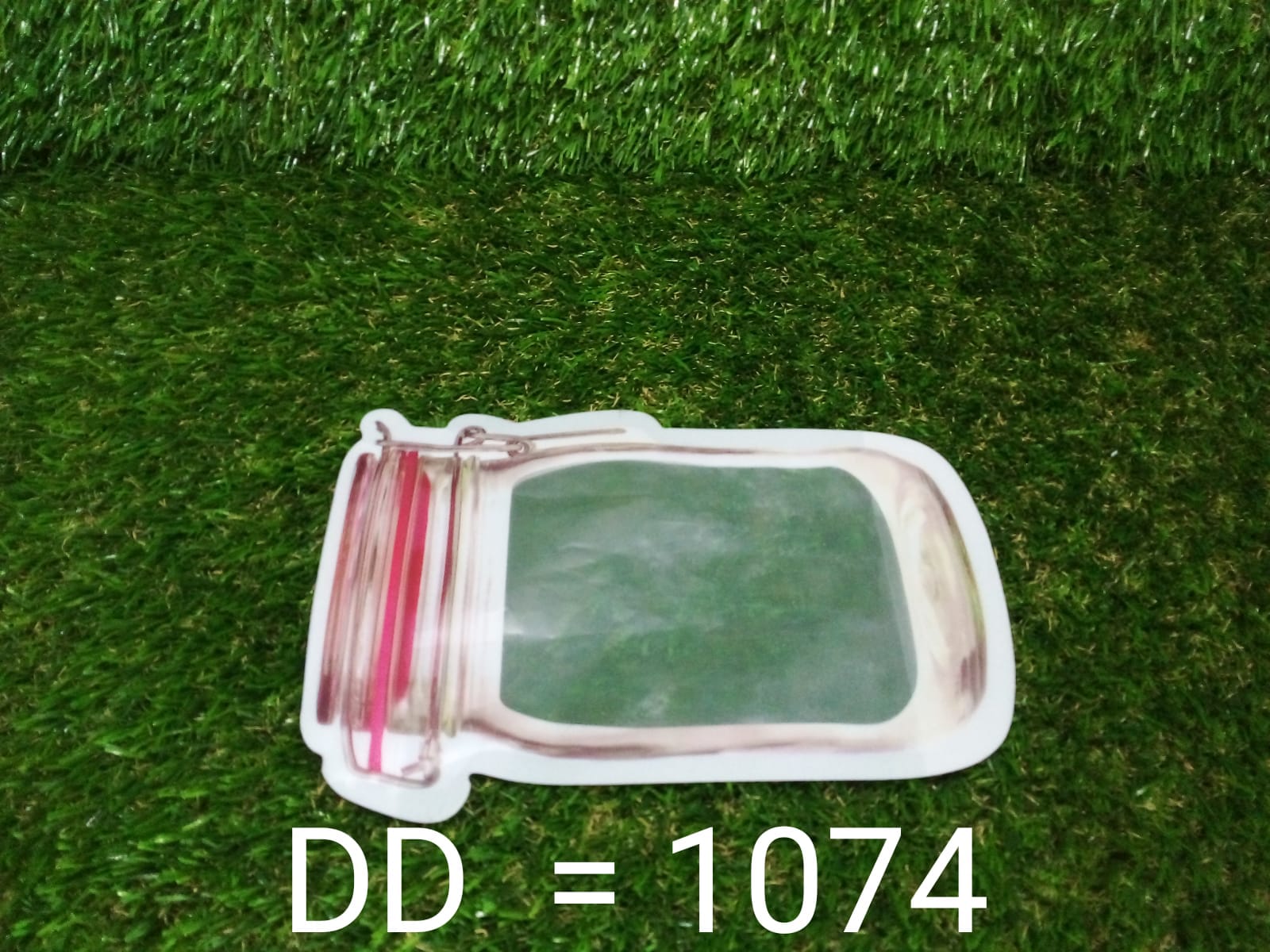 A jar-shaped zipper pouch lies horizontally on artificial green grass with the text "DD = 1074" below it.