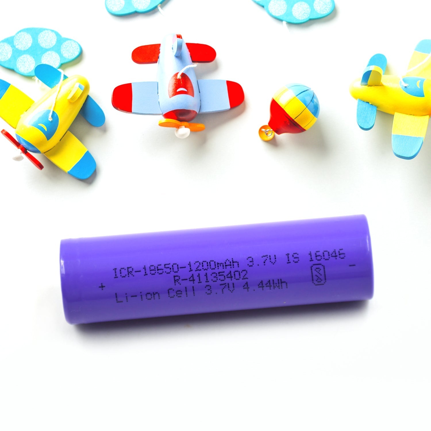 A purple battery lies on a white surface with colorful toy airplanes and clouds scattered around it.