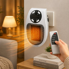 White and black wall heater plugged into an outlet, glowing orange, with a hand holding a remote control.