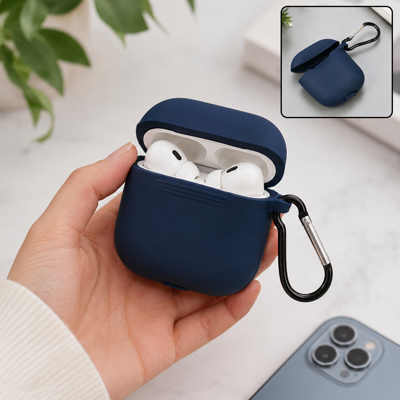A hand holds a navy blue silicone earbud case with white earbuds inside, next to a phone.