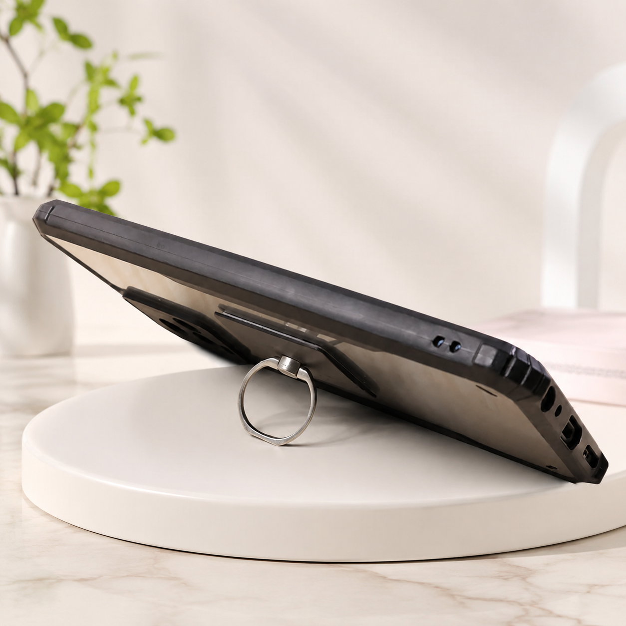 Black smartphone propped up on a white circular stand using a silver ring holder.