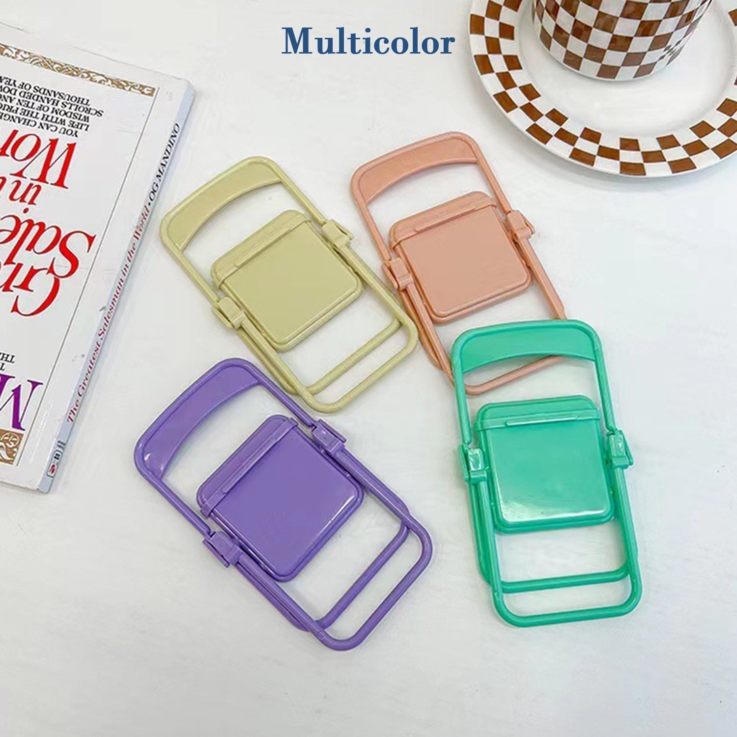 Four folded miniature chairs in purple, yellow, peach, and teal are arranged next to a patterned cup and book.