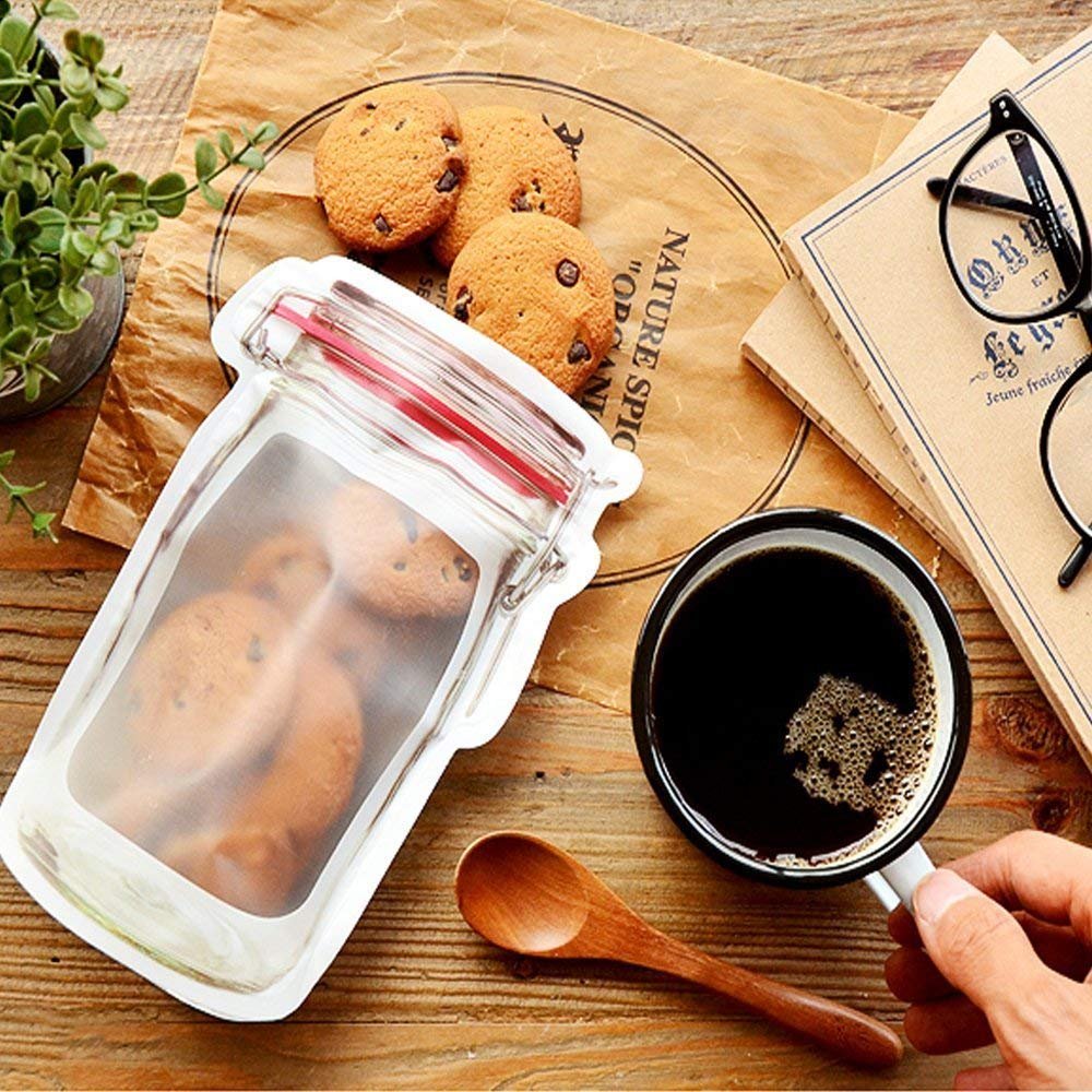 A jar-shaped zipper pouch filled with cookies rests on a brown paper with a cup of coffee and glasses.