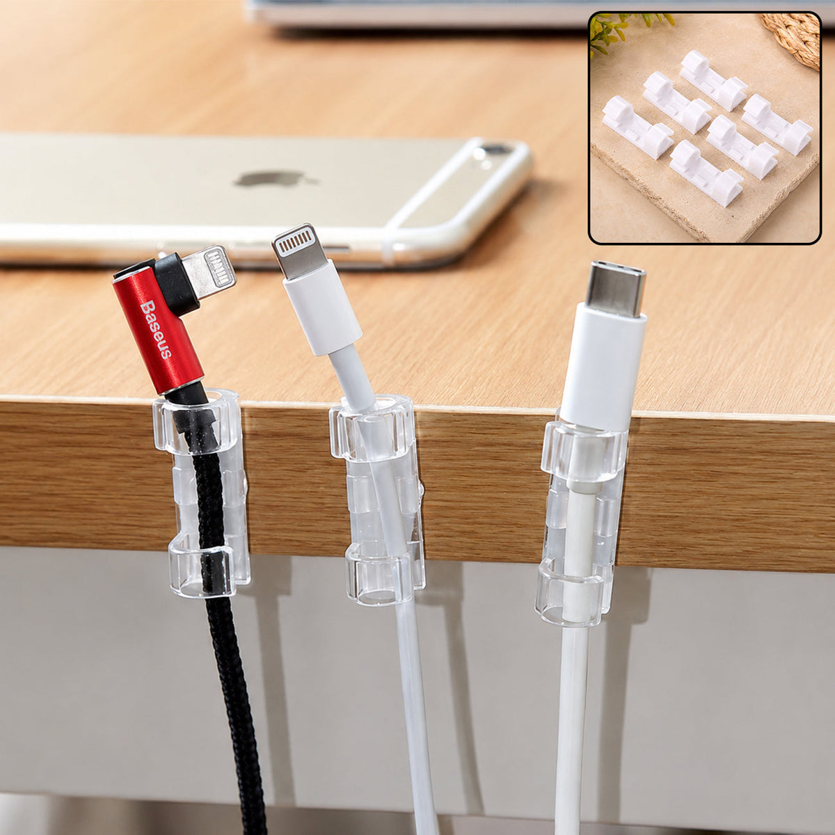 Three clear plastic cable clips holding a red, white, and black cable to the side of a wooden desk, with an iPhone and an