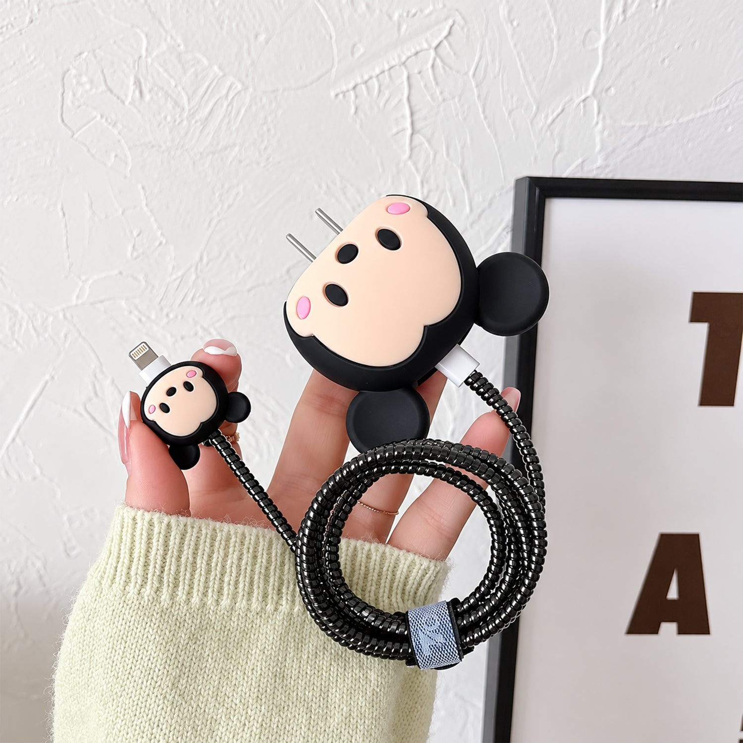 Hand holding a black Mickey Mouse charger cover with a striped cable protector and a matching small connector.
