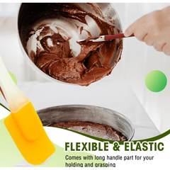 A yellow silicone spatula with a cream handle is partially visible, with a bowl of chocolate batter and a cake pan in the