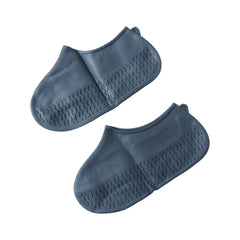 Two dark grey silicone shoe covers with textured soles are arranged on a plain white background.