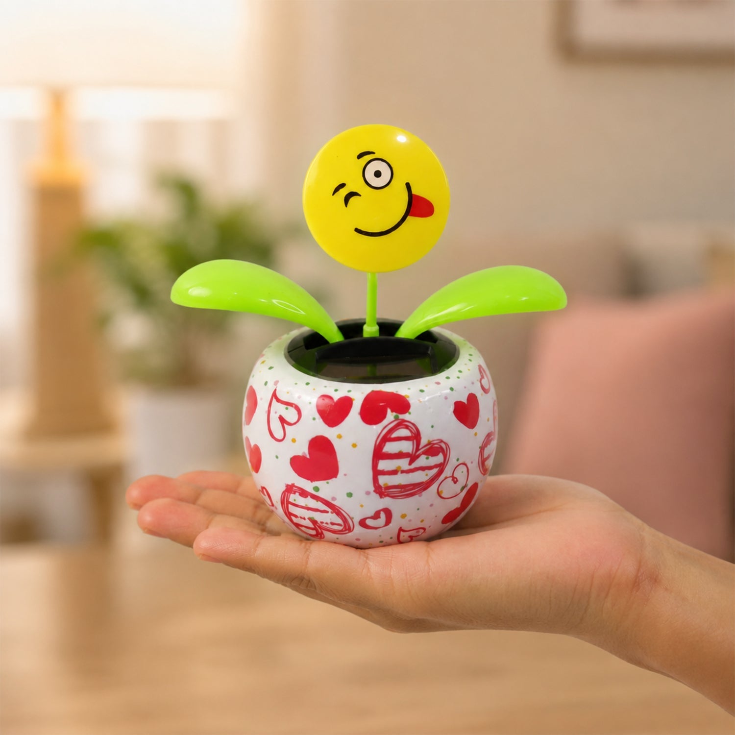 A person's hand holding a white pot with red hearts, containing a winking emoji face solar dancing flower.