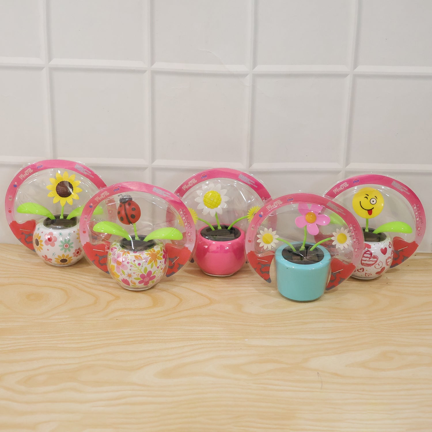 Five packaged solar dancing flowers in various designs, including a sunflower, ladybug, and winking emoji, on a wooden