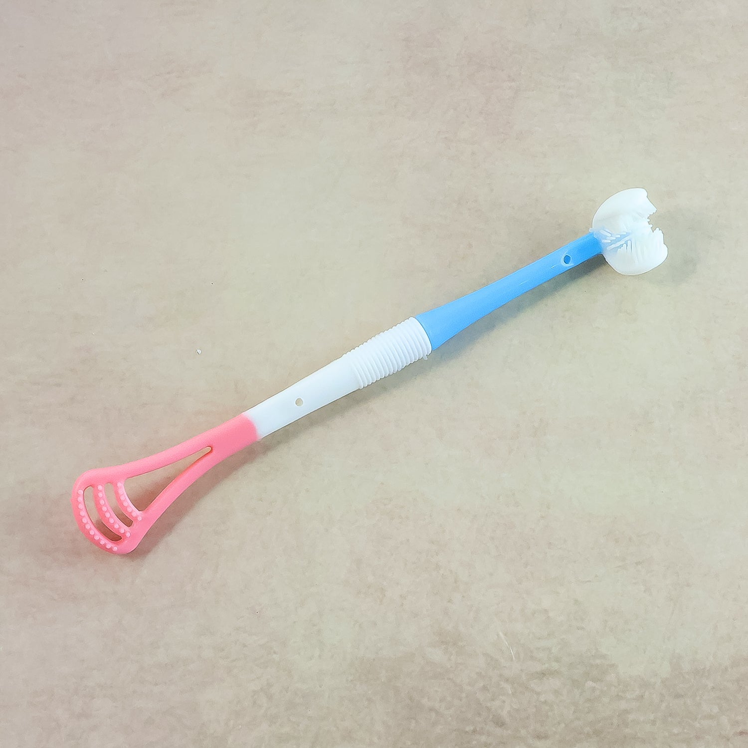 A blue, white, and pink baby tongue cleaner and toothbrush with a textured white handle and a pink scraper end.