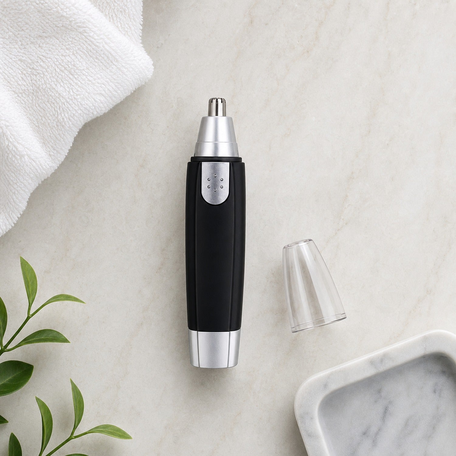 A black and silver nose hair trimmer with its clear cap removed lies on a white marble surface next to a white towel and