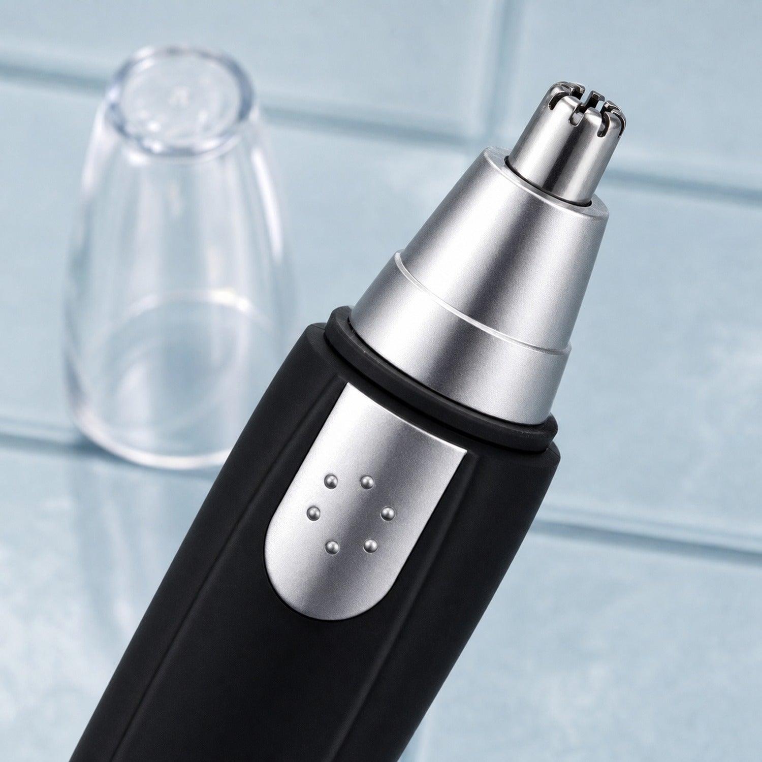 A close-up of the silver trimming head of a black and silver nose hair trimmer with its clear cap removed.