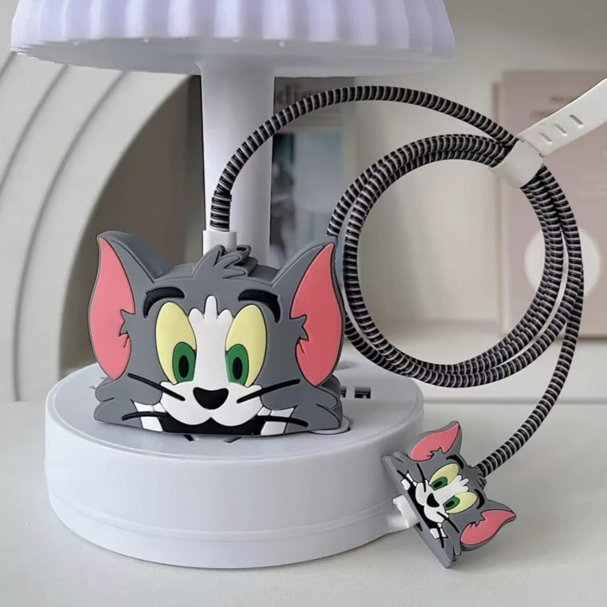 Gray Tom cat silicone charger cover with a striped cable protector on a white lamp base.