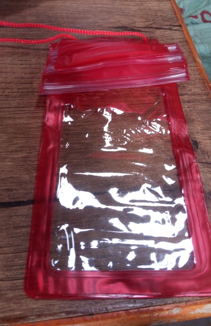 A red waterproof phone pouch with a clear front and red lanyard, lying on a wooden surface.