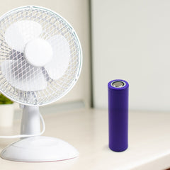 A purple battery stands next to a white desk fan on a light-colored table.